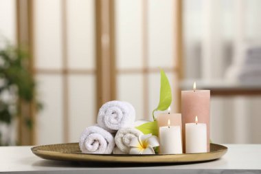 Spa kompozisyonu. Yanan mumlar, tesisat çiçeği, yeşil yapraklar ve havlular beyaz masa içinde, yazı için yer