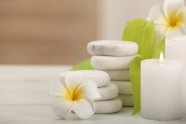 Spa kompozisyonu. Yanan mum, tesisat çiçekleri, beyaz masada taşlar ve yeşil yapraklar, yakın plan. Metin için boşluk