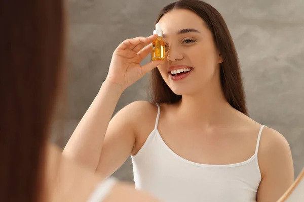 Happy young woman with essential oil near mirror