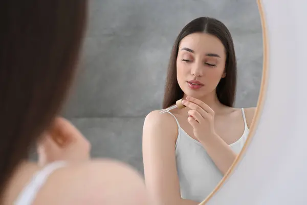Woman applying essential oil onto shoulder near mirror