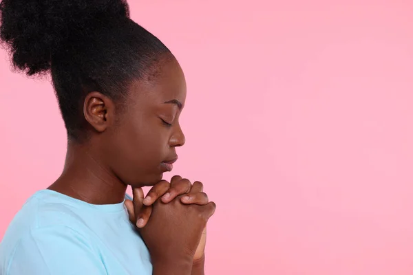 Woman with clasped hands praying to God on pink background. Space for text