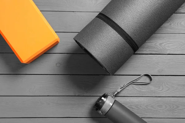 Exercise mat, yoga block and bottle of water on grey wooden floor, flat lay