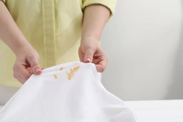 Woman holding shirt with stain at white table against light background, closeup. Space for text