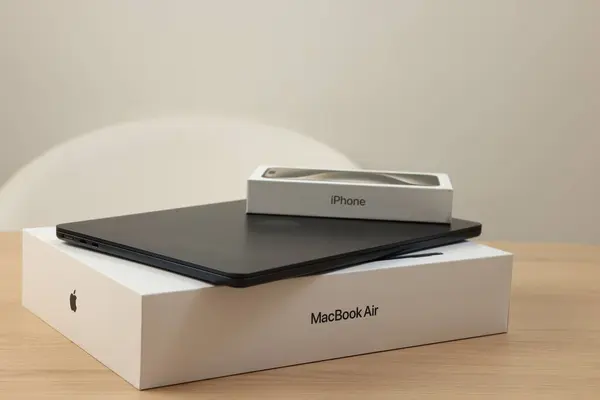 stock image Leiden, Netherlands - October 6, 2023: Modern black MacBook Air and box from iPhone 15 Pro Max on wooden table