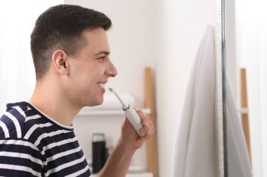 Adam banyoda aynanın yanında dişlerini elektrikli diş fırçasıyla fırçalıyor.