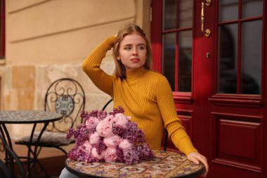 Açık kafede elinde bir buket bahar çiçeğiyle güzel bir kadın.