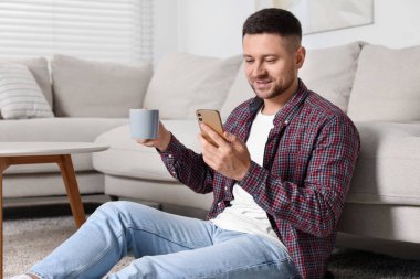Bir bardak içkiyle yakışıklı adam evde akıllı telefonla mesaj yolluyor.