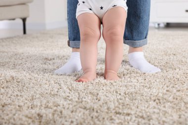 Anne, bebeğine evde halıda yürümeyi öğrenirken destek oluyor.