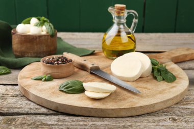 Lezzetli mozzarella dilimleri, fesleğen yaprakları, bıçak ve baharatlar ahşap masada.