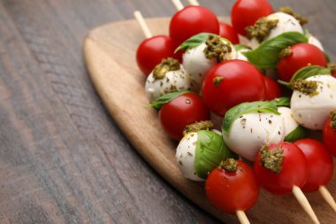 Domatesli Caprese şişleri, mozzarella topları, fesleğen ve pesto sosu ahşap masada, yakın plan. Metin için boşluk