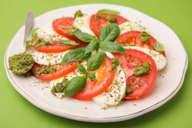 Bir tabak lezzetli Caprese salatası ve yeşil masada pesto soslu kaşık, yakın plan.