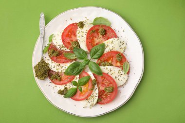 Bir tabak lezzetli Caprese salatası ve yeşil masada pesto soslu kaşık.