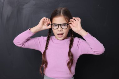 Okula dönelim. Kara tahtanın yanında gözlüklü şirin bir kız.