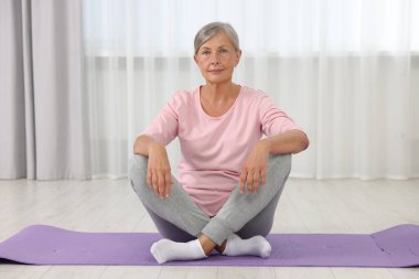 Evde paspasın üzerinde oturan yaşlı kadın. Yoga alıştırması.