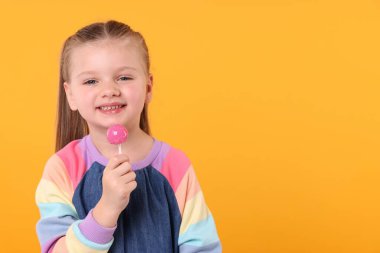 Turuncu arka planda lolipopu olan mutlu küçük kız, mesaj için yer.