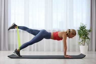 Spor yapan atletik bir kadın evde spor yaparken lastikli bant takıyor.