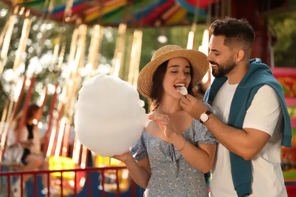 Young man feeding his girlfriend with cotton candy at funfair