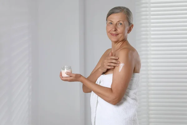 Happy woman applying body cream onto arm indoors. Space for text