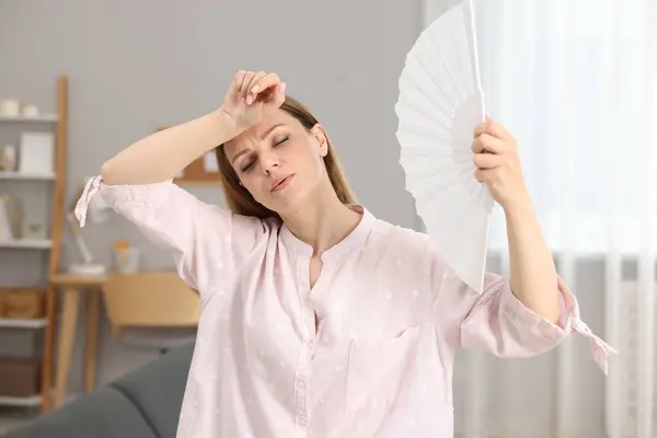 stock image Woman waving white hand fan to cool herself at home