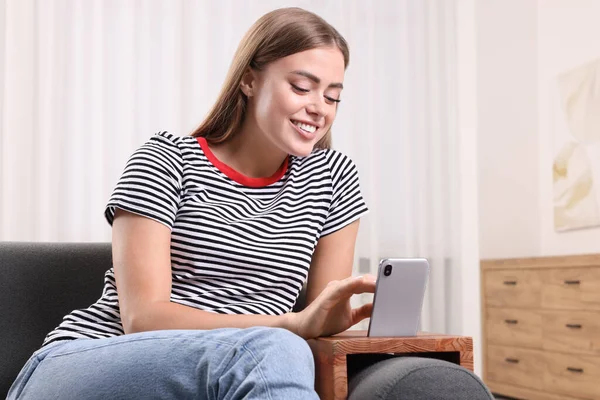 Happy woman using smartphone on sofa armrest wooden table at home