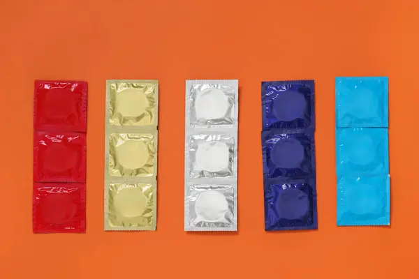 Packaged condoms on orange background, flat lay. Safe sex