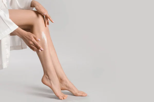 Woman applying body cream onto her smooth legs on light grey background, closeup. Space for text