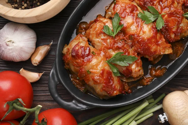 Delicious stuffed cabbage rolls cooked with tomato sauce and ingredients on wooden table, flat lay