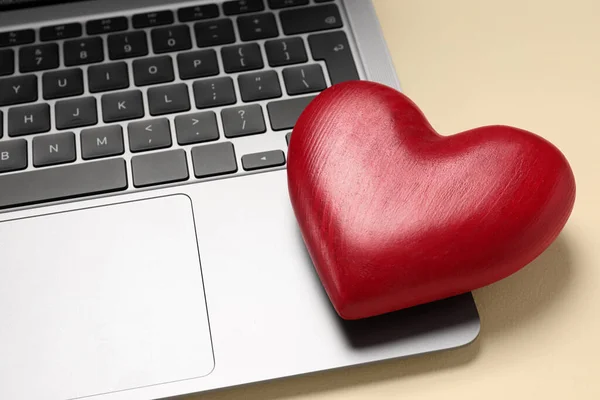 Long-distance relationship concept. Laptop and decorative heart on beige background, closeup