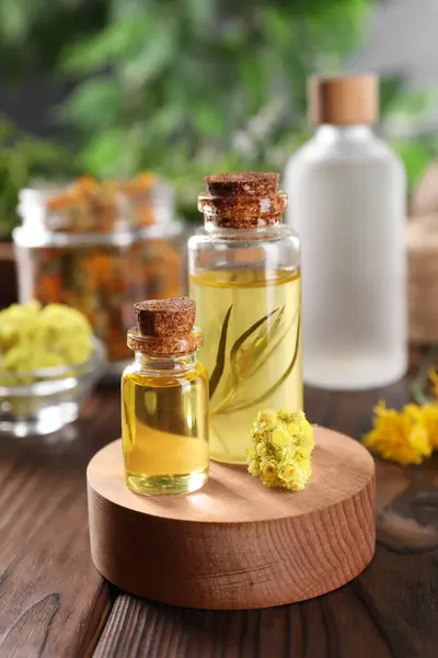 Bottles of essential oils and dry herbs on wooden table