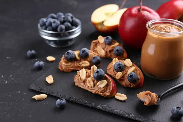 Fresh apples with peanut butter and blueberries on dark table