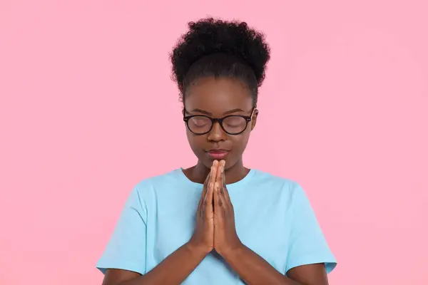 Woman with clasped hands praying to God on pink background