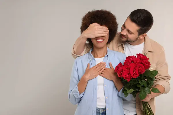 International dating. Handsome man presenting roses to his beloved woman on light grey background, space for text