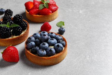 Açık gri masada farklı taze böğürtlenli turtalar, yazı için yer. Tatlı nefis.