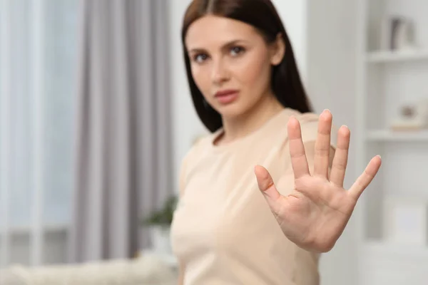 Woman showing stop gesture at home, selective focus. Space for text