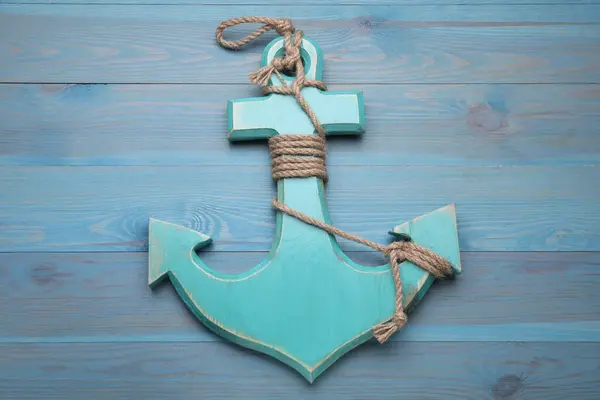 Anchor with hemp rope on light blue wooden table, top view