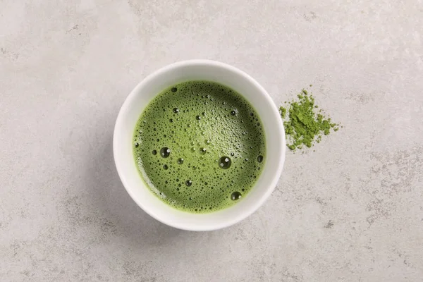 Cup of matcha tea on light gray textured table, top view