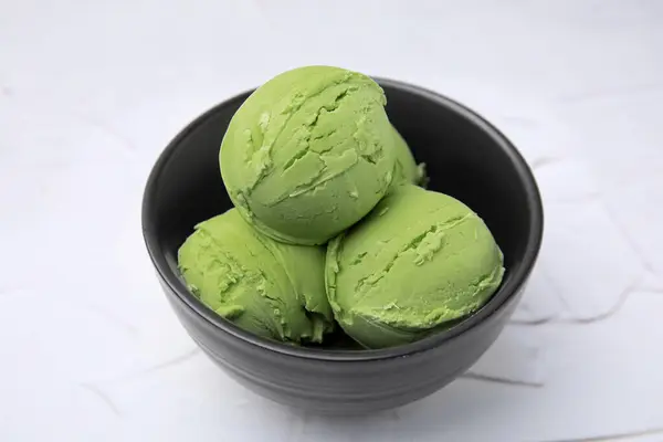 Tasty matcha ice cream in bowl on white textured table