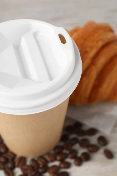 Coffee to go. Paper cup with tasty drink, croissant and beans on white table, closeup