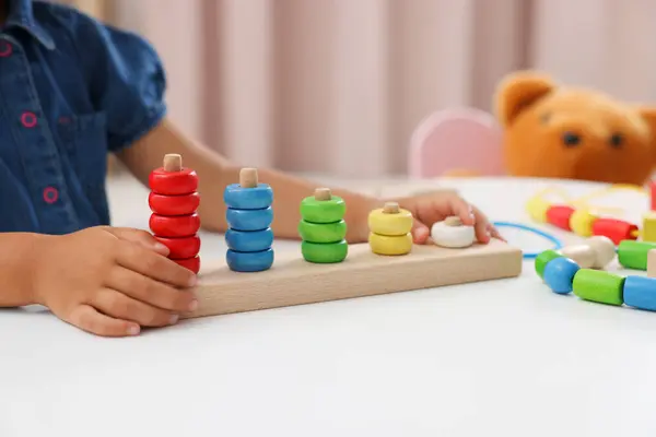 Motor skills development. Little girl playing with stacking and counting game at table indoors, closeup