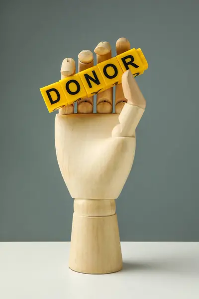 Mannequin hand holding word Donor made of cubes on white table against grey background
