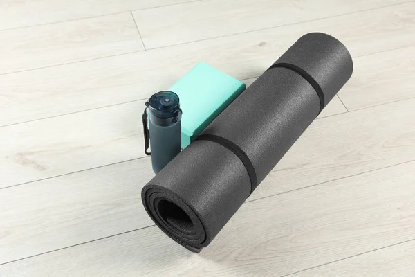 Exercise mat, yoga block and bottle of water on light wooden floor