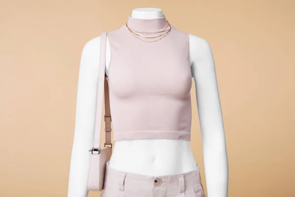 Female mannequin with bag dressed in stylish crop top and pants on beige background