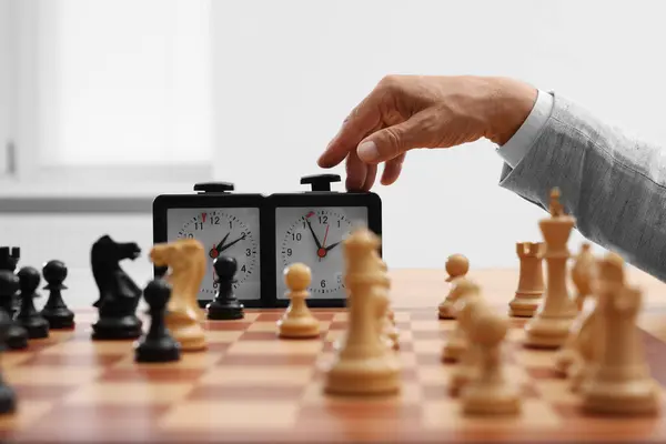 Man turning on chess clock during tournament at chessboard, closeup