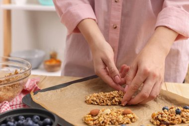 Tahıl gevreği yapıyorum. Yulaf gevreği, kuru meyve ve diğer malzemelerin karışımını mutfaktaki yemek tepsisine koyan kadın, yakın plan.