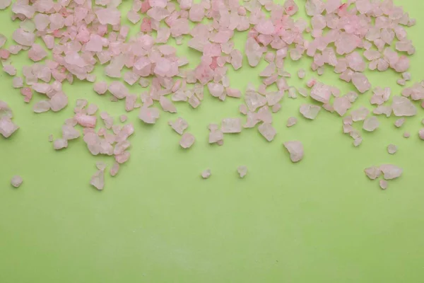 Pink sea salt on light green background, top view. Space for text