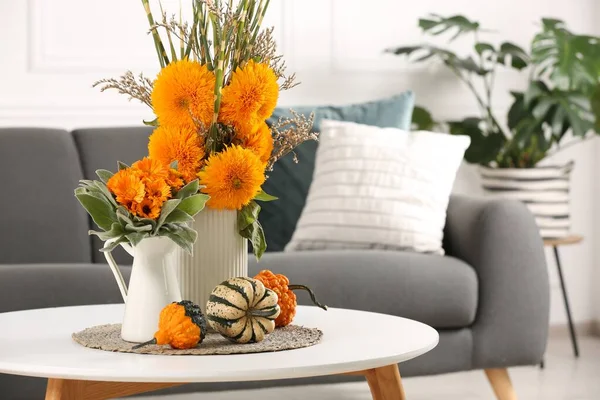 Beautiful autumn bouquets and pumpkins on coffee table near sofa in room