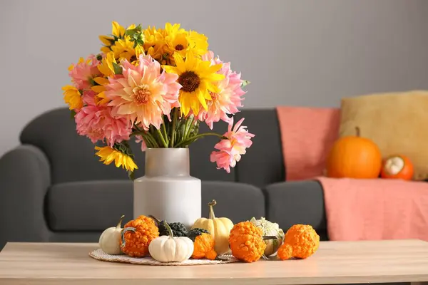 Autumn mood. Beautiful bouquet with bright flowers and small pumpkins on wooden table in room, space for text
