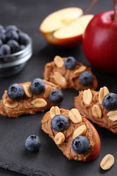 Fresh apples with peanut butter and blueberries on dark table, closeup