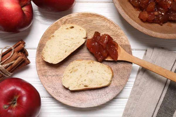 Delicious apple jam and bread slices on white wooden table, flat lay