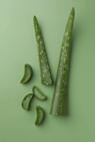 Cut aloe vera leaves on green background, flat lay
